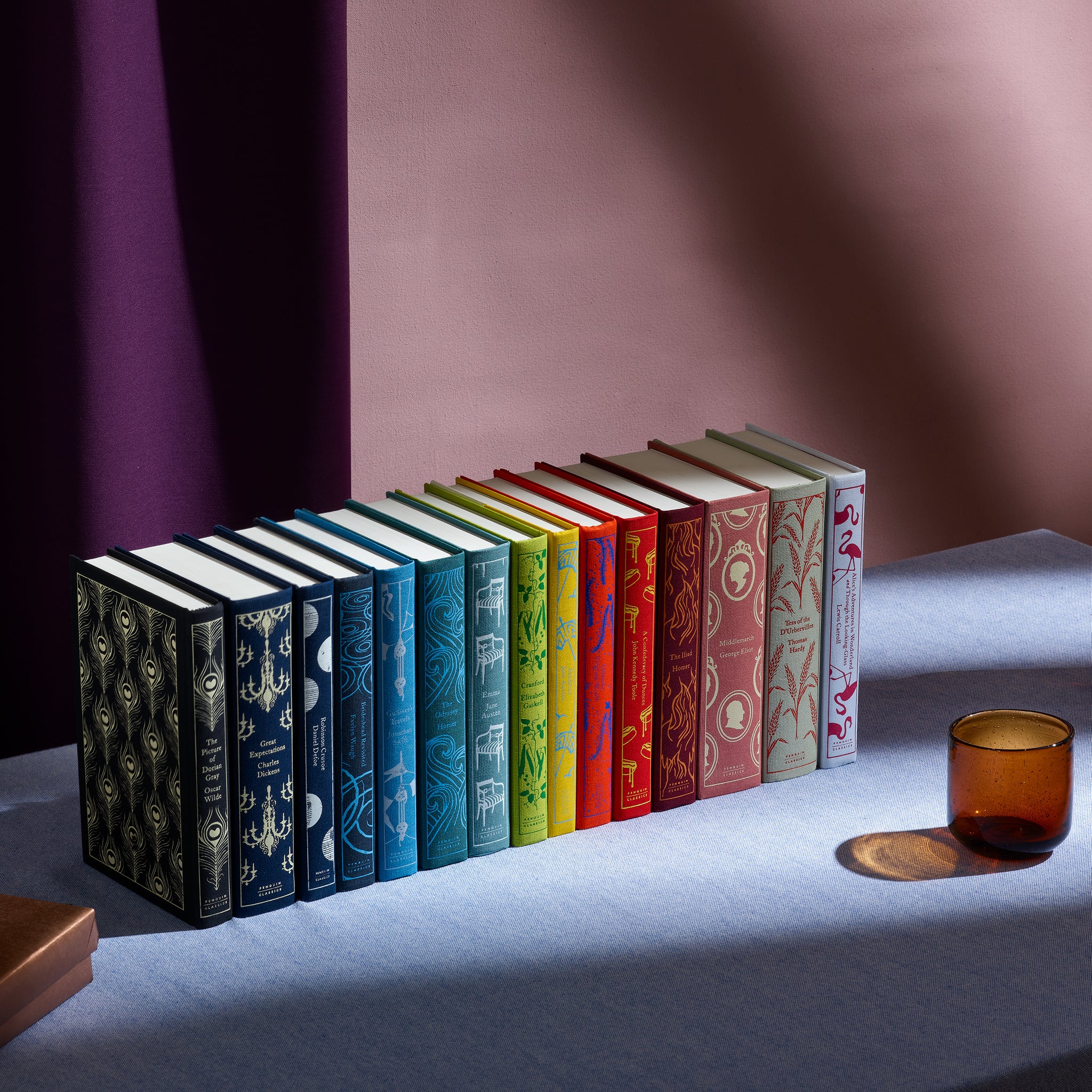 Penguin Clothbound Classics stacked in a row on a blue clothed table with a glass