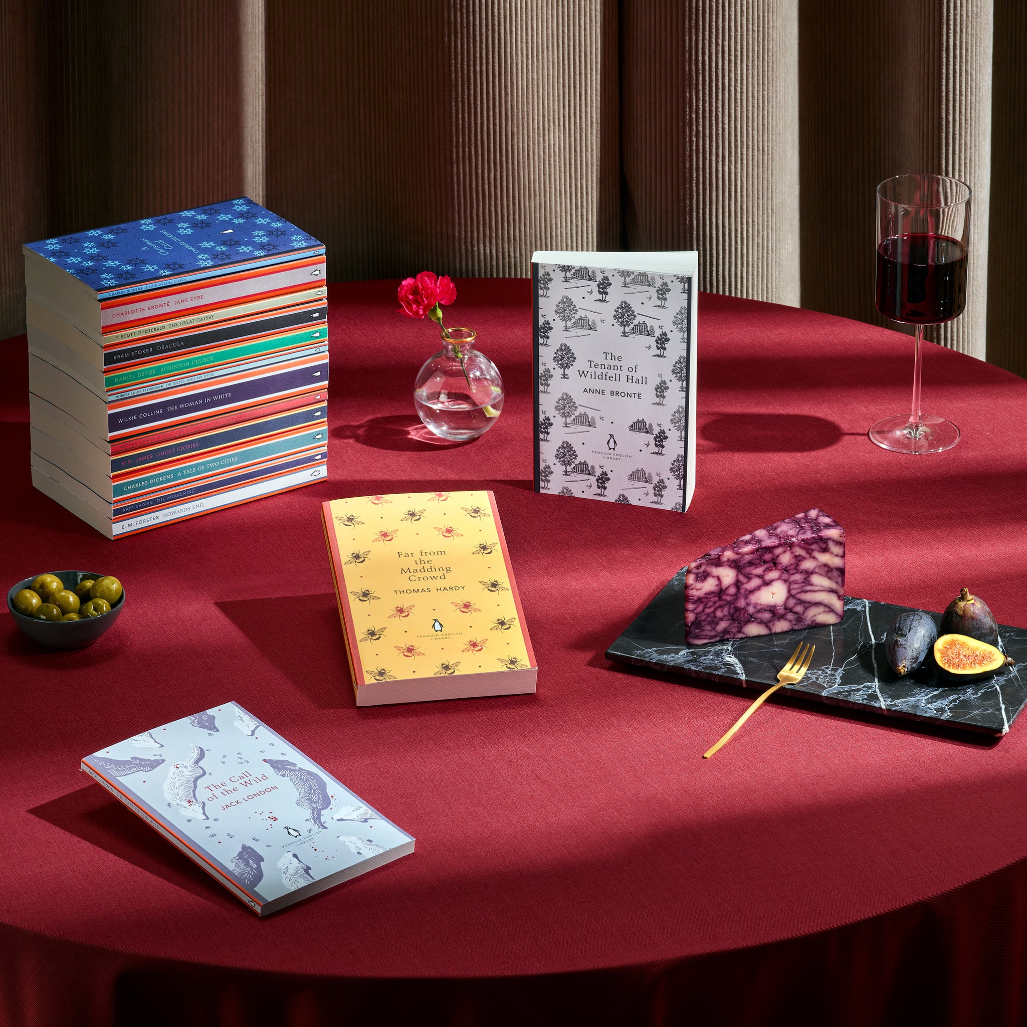 Penguin English Library stacked and scattered on a red clothed table with food and drink