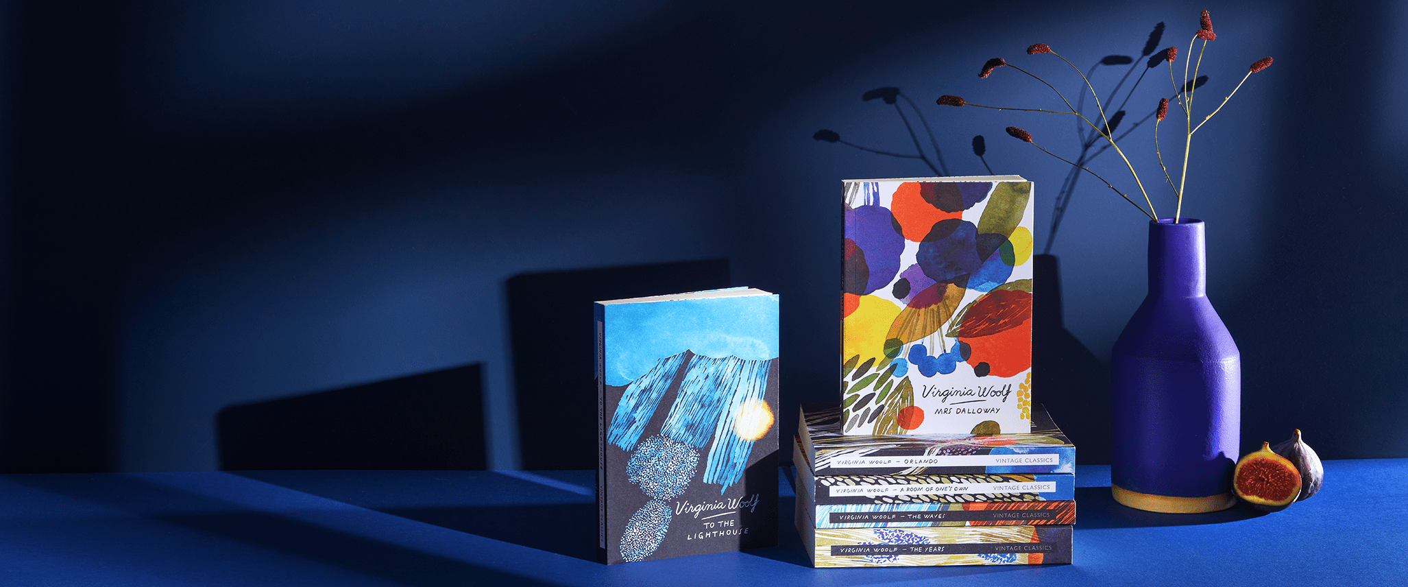 Vintage Virginia Woolf book collection on a blue background with a vase and a fig
